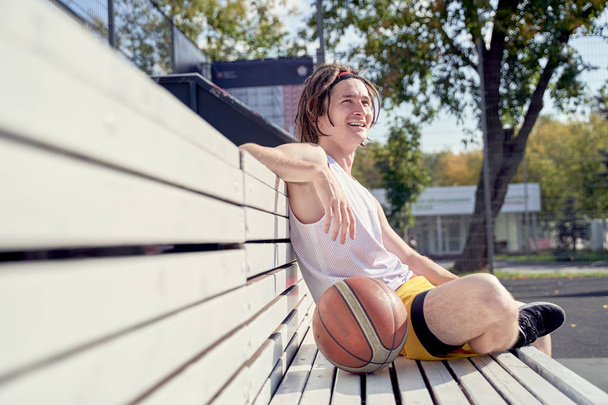 Picture of sporty man with volleyball ball sitting on wooden bench on summer. - Fotografie, Obrázek