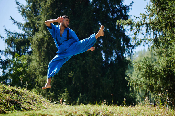 Aziatische Kazachse Karate Fighter is Combat in blauwe kimono uniform op een zomer prachtige natuur landschap met Kopieer ruimte - Foto, afbeelding