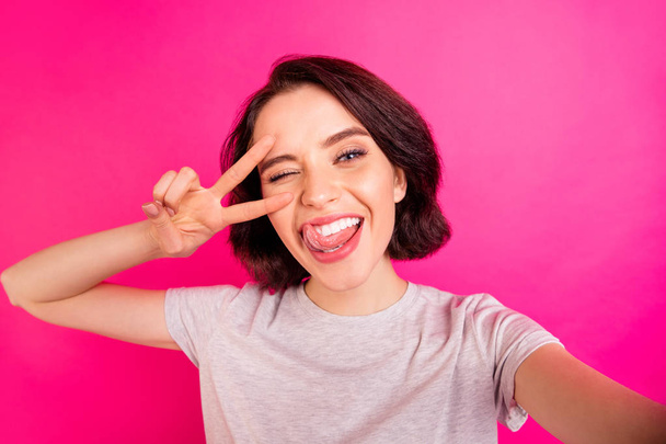 Self photo of charming cute nice attractive pretty sweet girlfriend licking her lips blinking taking selfie showing you v-sign near winking eye while isolated over pink color vivid background - Zdjęcie, obraz