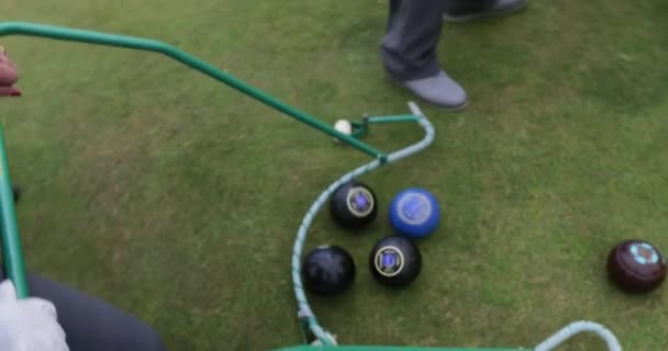 A senior man can be seen collecting a group of bocce balls using a pick up tool at a bowling green. - Footage, Video