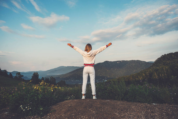 Happy celebrating winning success woman in white clothes standing elated with arms raised up above head in celebration of having reached mountain top summit goal during hiking travel trek. - Photo, Image