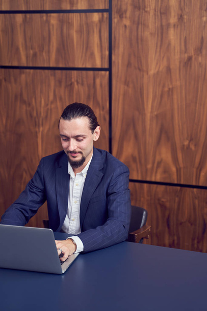 Image of businessman sitting at table with laptop on background of wooden wall. - Valokuva, kuva