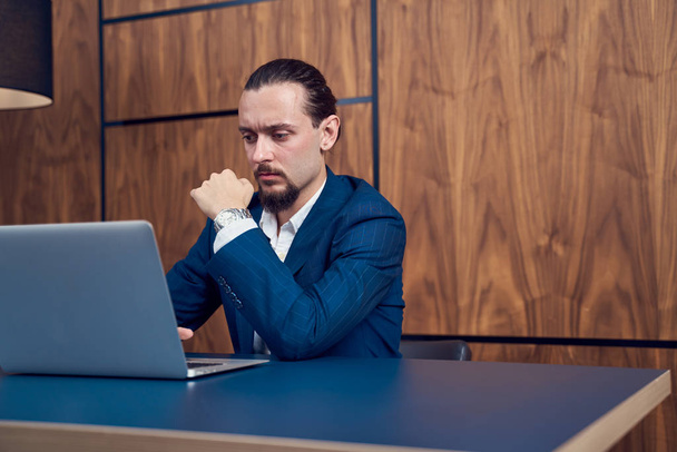 Photo on side of businessman sitting at table with laptop on background of wooden wall. - 写真・画像