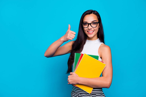 Photo of pretty lady holding study book in arms diligent student raising thumb up wear specs white tank-top and striped skirt isolated blue color background - 写真・画像