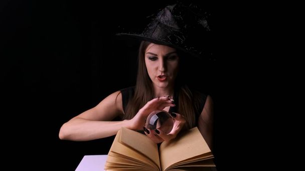 mujer sexy en un traje de bruja negro y sombrero, sostiene una bola mágica transparente en sus manos y evoca. Fiesta de Halloween
. - Foto, imagen