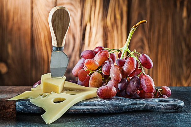 maasdam cheese knife on little cutting board and rose grape on w - Foto, Imagem