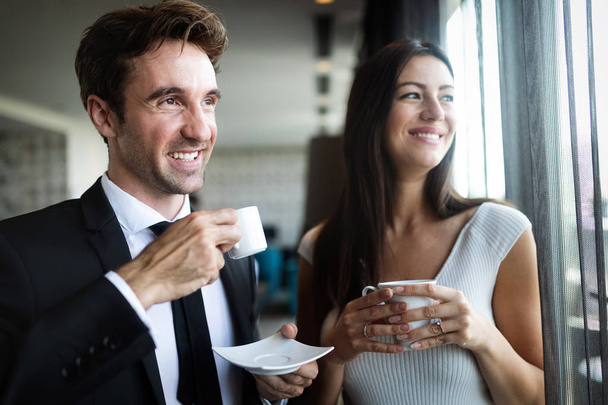 Coffee break. Couple of young colleagues in formal wear standing at workplace, drinking coffee near window - Φωτογραφία, εικόνα
