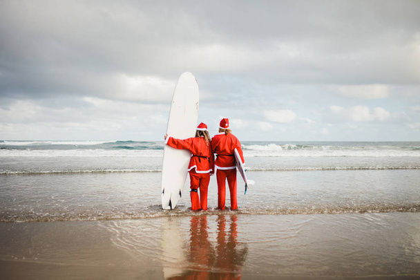 dwóch surferów przebranych za Świętego Mikołaja na plaży - Zdjęcie, obraz