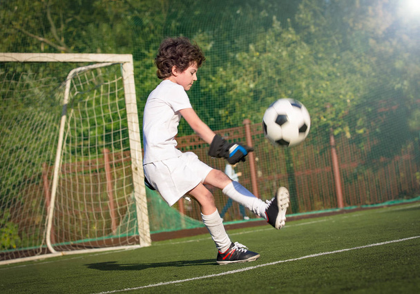 Boy in white sportswear running on soccer field. Young footballer dribble and kick football ball in game. Training, active lifestyle, sport, child activity concept. selective focus - Foto, Imagen
