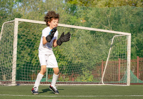 Summer soccer tournament for young kid. Football club. Emotions and joy of game. Young goalie. Kid - soccer champion. Boy goalkeeper in football sportswear on stadium with ball. Sport concept. - Foto, Imagen
