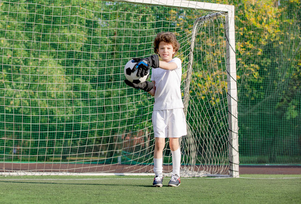 Futbol sahasında koşan beyaz giysili bir çocuk. Genç futbolcu futbolda top sürüyor ve topa vuruyor. Eğitim, aktif yaşam tarzı, spor, çocuk aktivitesi konsepti. seçici odak - Fotoğraf, Görsel