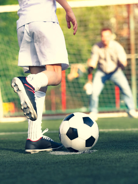 Ένα αγοράκι με τον μπαμπά του να παίζουν ποδόσφαιρο στο γήπεδο. Παιδικός ποδοσφαιριστής ετοιμάζεται να ρίξει σε γήπεδο ποδοσφαίρου. - Φωτογραφία, εικόνα