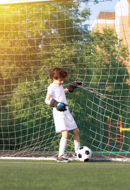 Boy in white sportswear running on soccer field. Young footballer dribble and kick football ball in game. Training, active lifestyle, sport, child activity concept. selective focus - Photo, image