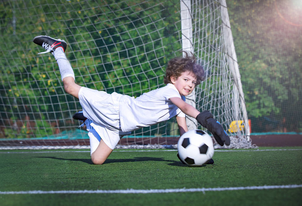 Young soccer goalie attempting to make a save. Little soccer goalkeeper with gloves. Kid - soccer champion. Boy goalkeeper in football sportswear on stadium with ball. Sport concept. - Fotografie, Obrázek