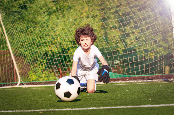 Summer soccer tournament for young kid. Football club. Emotions and joy of game. Young goalie. Kid - soccer champion. Boy goalkeeper in football sportswear on stadium with ball. Sport concept. - Foto, Imagem