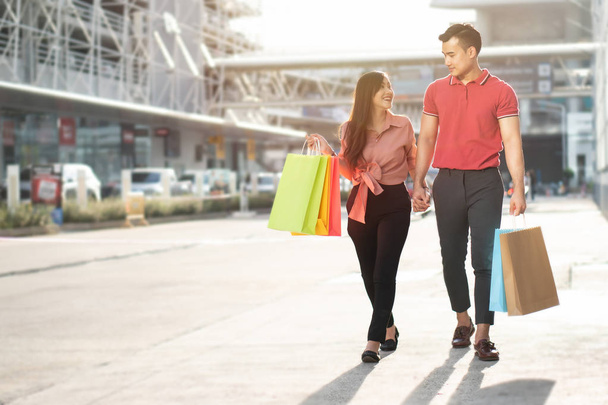 Feliz casal jovem de compradores andando na rua comercial e segurando sacos de compras coloridos na mão. Conceito de venda e compras na sexta-feira preta - Foto, Imagem