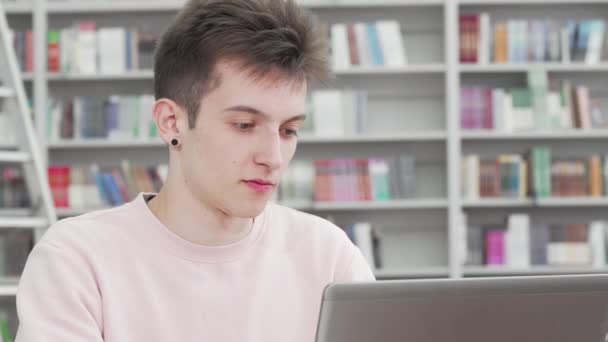 Gesneden foto van een jonge mannelijke student glimlachend naar de camera in de bibliotheek - Video