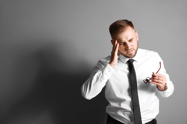 Young businessman suffering from headache on grey background - Foto, imagen