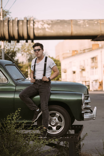 Guy in a shirt with suspenders posing at the retro car - Foto, imagen