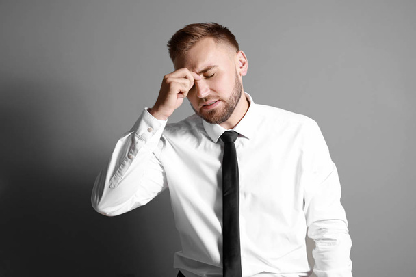 Young businessman suffering from headache on grey background - Фото, изображение