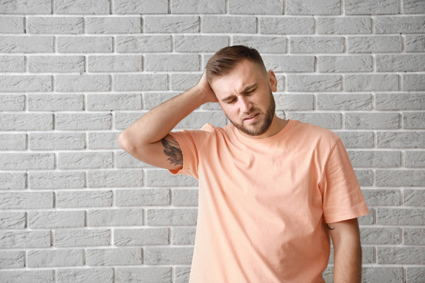 Młody człowiek cierpiący na ból głowy przy szarej ceglanej ścianie - Zdjęcie, obraz