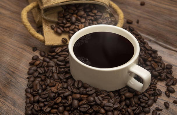 Cup of coffee beans and burlap sack on wooden background, copy space banner - 写真・画像