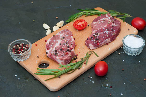 Carne crua sobre tábua de corte, polvilhada com sal e pimenta, alho, alecrim e tomate, vista superior e vista lateral
 - Foto, Imagem