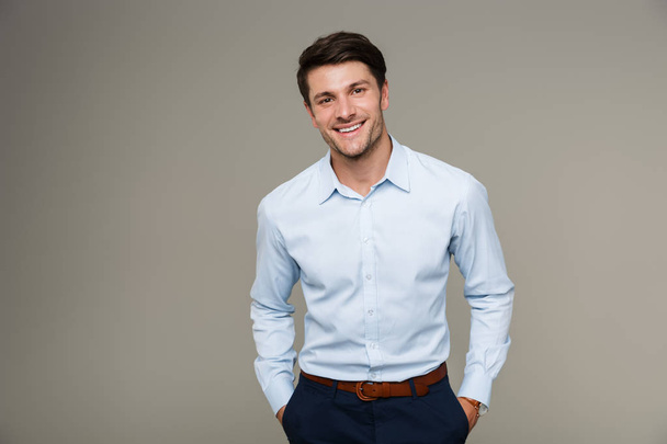 Image of happy brunette man wearing formal clothes smiling at camera with hands in pockets - Photo, Image