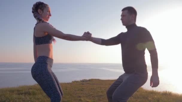 aktivní životní styl, atletický pár držící se za ruce a současně krčící se v přírodě - Záběry, video