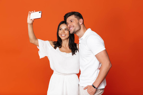 Happy positive pleased young amazing loving couple posing isolated over red wall background take selfie by mobile phones. - Fotó, kép