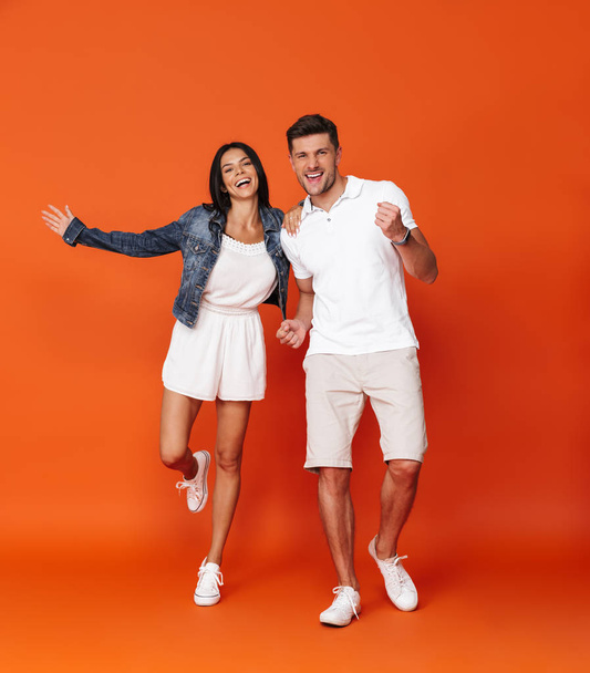 Optimistic cheerful amazing loving couple posing isolated over red wall background make winner gesture. - Foto, Imagen