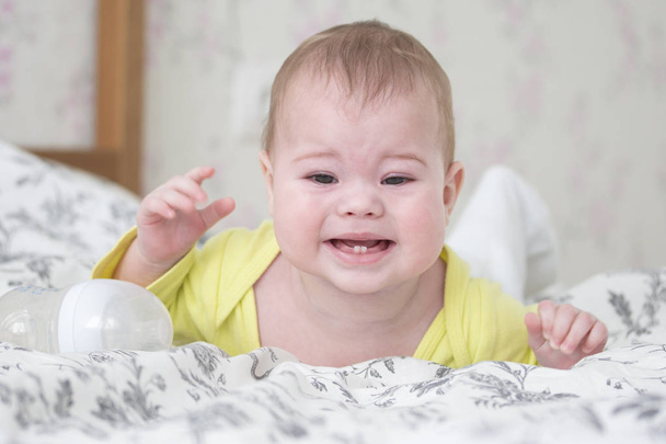 Bebé de 6 a 7 meses llorando acostado boca abajo. Un bebé caucásico en amarillo está llorando y mostrando 2 dientes de bebé, dentición, enfoque suave retrato
 - Foto, Imagen