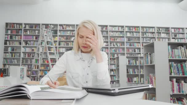 Kaunis naispuolinen opiskelija korostaa opiskellessaan kirjastossa
 - Materiaali, video