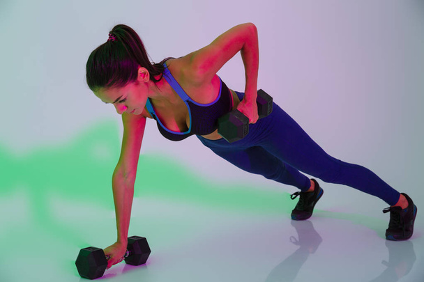 Attractive young fitness woman isolated with led flash lights make exercises with dumbbells for arms. - Foto, immagini