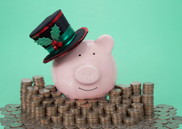 Różowy świnka bank sobie Holiday urządzone top kapelusz uśmiechnięty widz stoi otoczony stosy monet, zielone tło. - Zdjęcie, obraz