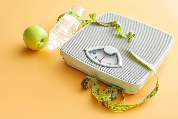 Scales, apple, measuring tape and bottle of water on color background. Weight loss concept - Photo, Image