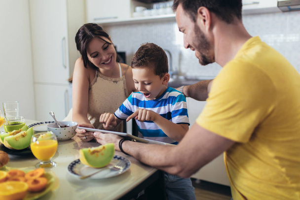 キッチンテーブルで朝食を食べ、デジタルテーブルを使用する家族 - 写真・画像