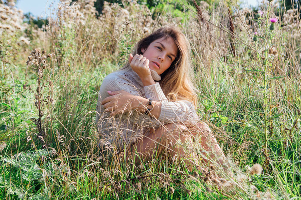 Boldog fiatal, gyönyörű nő pulóverben és alsónadrágban ül mezítláb egy száraz mezőn. - Fotó, kép