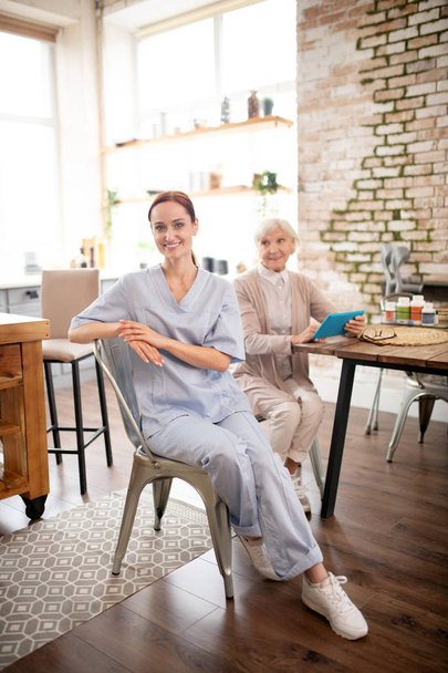 Caregiver wearing uniform and sneakers visiting pensioner - Fotografie, Obrázek