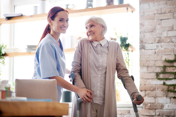 Woman with crutches smiling while talking to caregiver - Foto, immagini