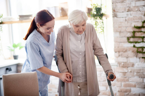 Helpful caregiver assisting woman with crutches - Photo, image