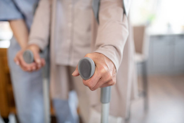 Close up of retired woman holding crutches while walking - Zdjęcie, obraz