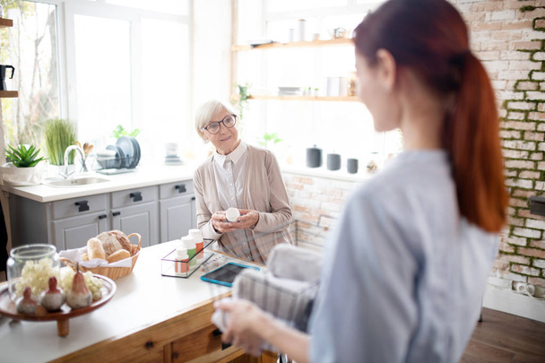 Retired woman wearing glasses talking to her caregiver - Foto, imagen