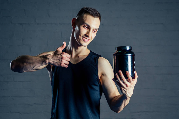 a young man holding a jar of protein in the gym - Foto, Bild