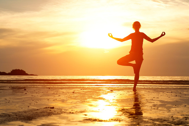 Backlit, young woman practicing yoga on the beach at sunset. - Photo, Image