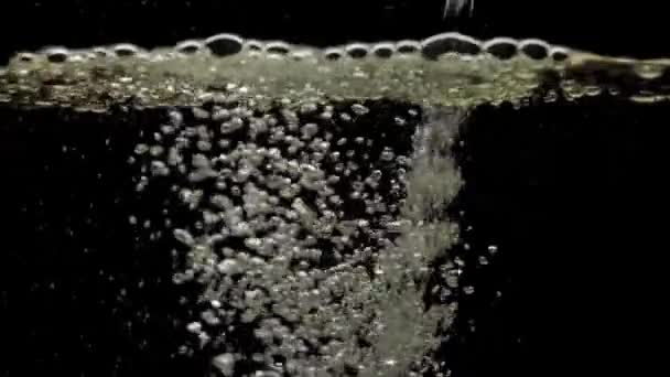 Na černé pozadí kape proud vody. Křišťálově čistý průtok vody dopadá na povrch a vytváří vzduchové bubliny s kopírovacím prostorem. Zpomal. Detailní záběr. - Záběry, video
