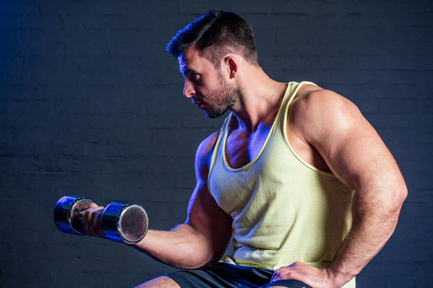 jovem e belo atleta atleta homem fisiculturista fazendo exercícios para os músculos das mãos de halteres no ginásio
 - Foto, Imagem
