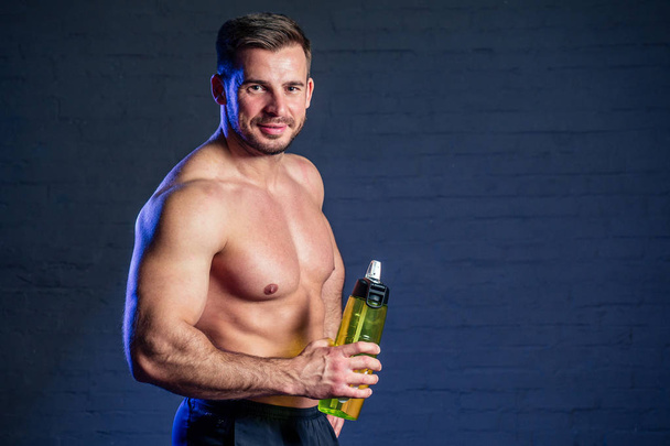Genç ve yakışıklı seksi çıplak adam spor salonunda bir şişe su tutuyor. Sağlıklı yaşam tarzı ve vücut geliştirme kavramı - Fotoğraf, Görsel