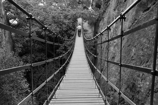 Літній чоловік ходить по підвісному мосту з залізних і дерев'яних дощок
 - Фото, зображення