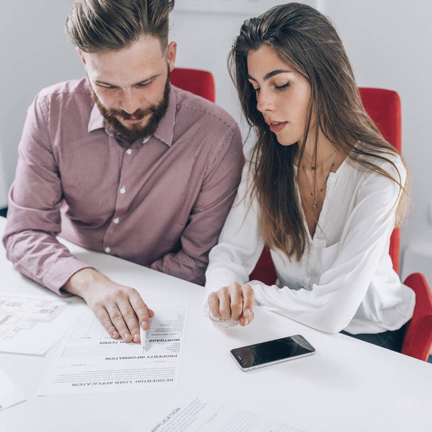 Satisfait jeune couple lire et se préparer à signer un contrat hypothécaire dans le bureau de l'agence immobilière
. - Photo, image
